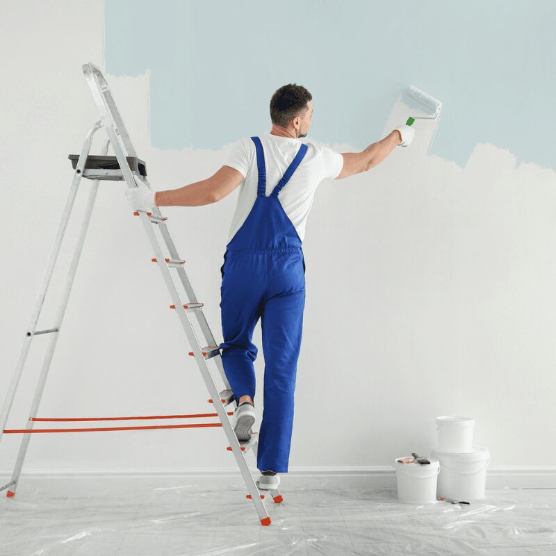man painting high wall using ladder